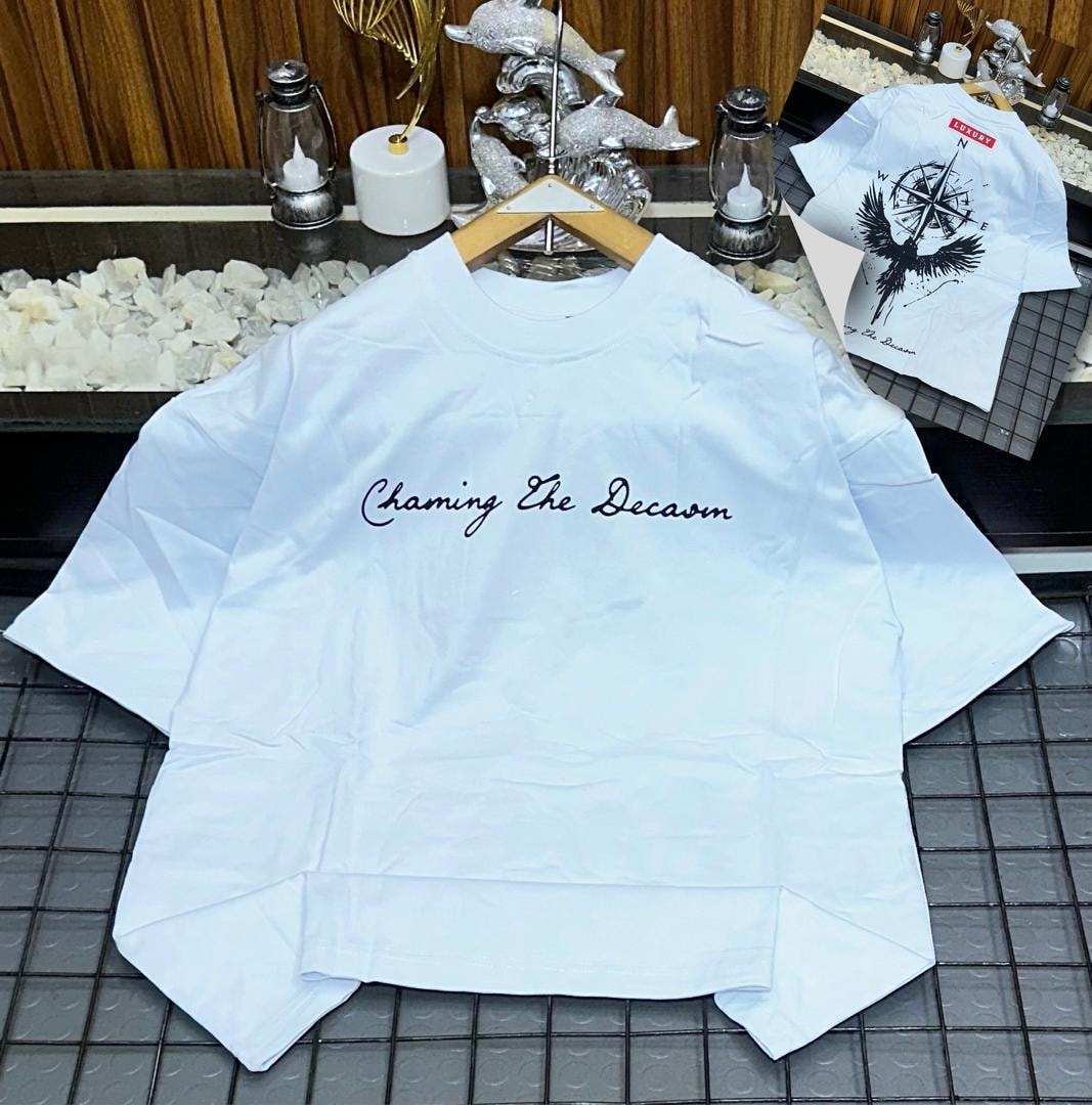 White oversized t-shirt with black cursive 'Chaming The Decaom' print on front and inset bird compass back view.
