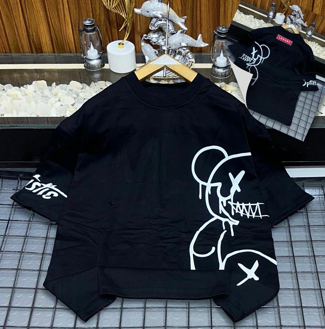 Black oversized t-shirt with large white character graphic on front and sleeve text, shown on hanger with back view.
