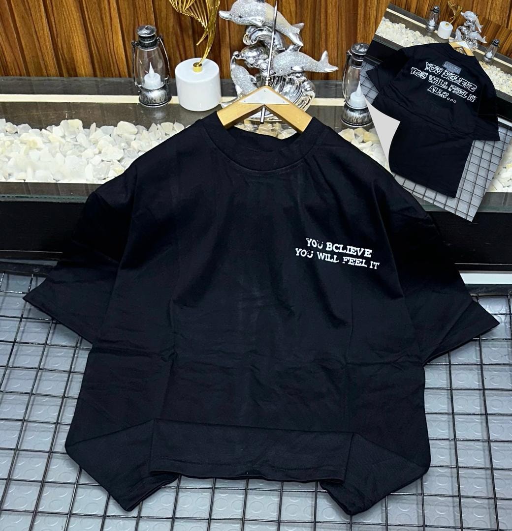 Black oversized t-shirt with white text print 'YOU BELIEVE YOU WILL FEEL IT' on chest, shown on hanger with back view.