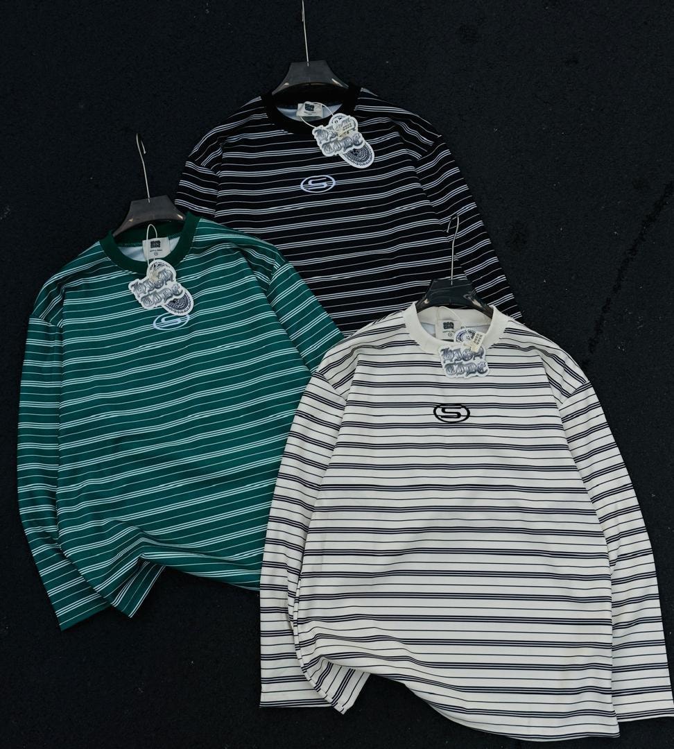 Three long sleeve striped tops in green, black and white displayed together on dark background.