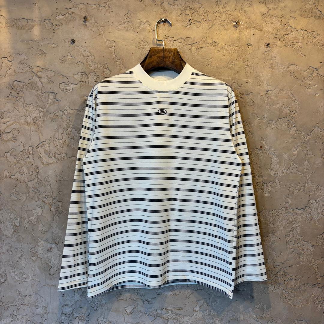 White and black horizontally striped long sleeve top on hanger against textured wall.