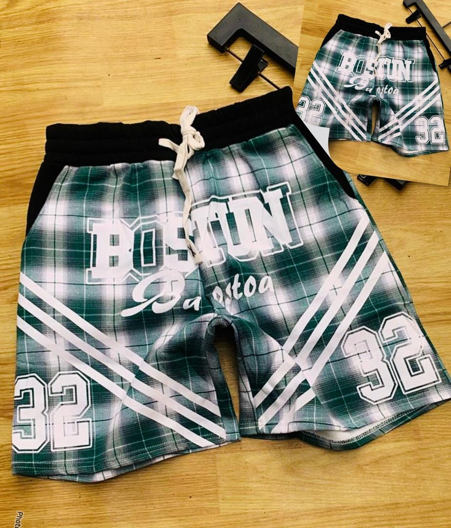 Green plaid Boston graphic shorts with white stripes on wooden background.