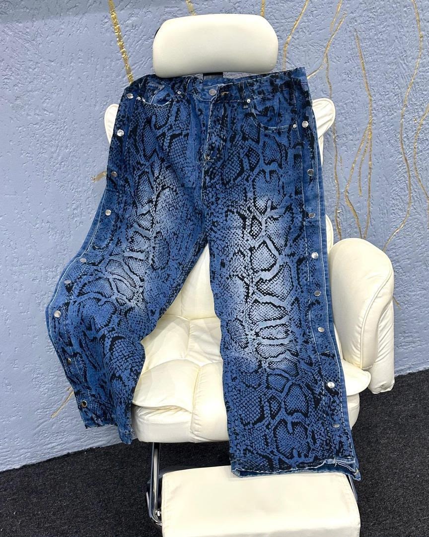 Blue snake print baggy jeans with silver studs displayed on white chair.