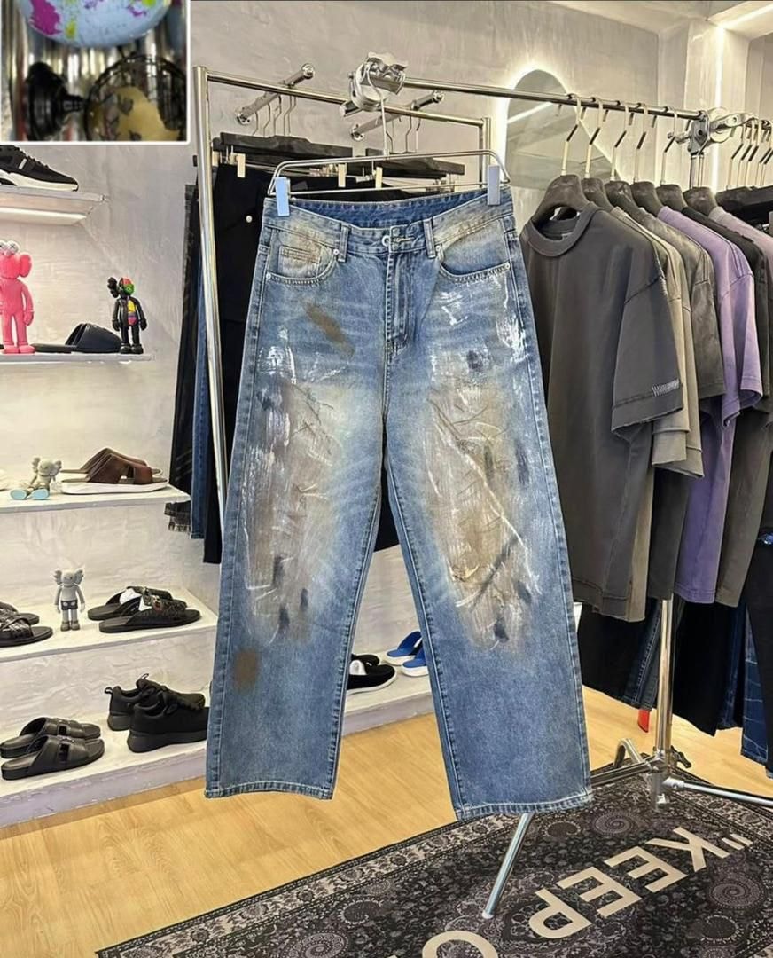 Blue baggy jeans with heavy paint strokes hanging on rack in store.