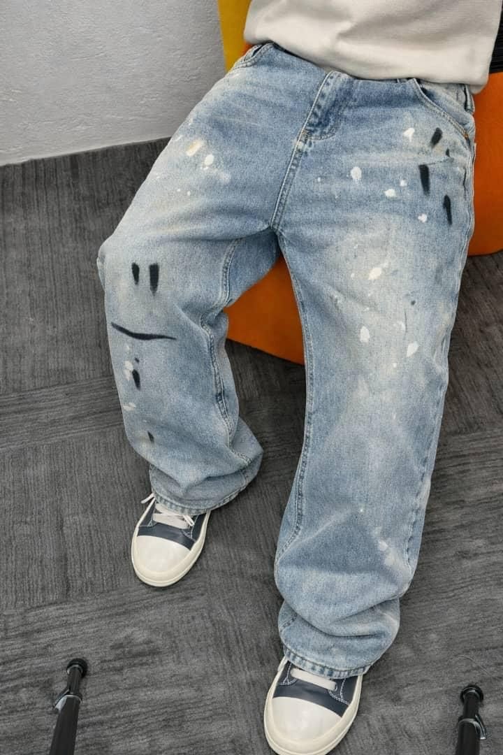 Light blue baggy jeans with smiley face paint design, black and white splatters, worn seated with white and blue sneakers.