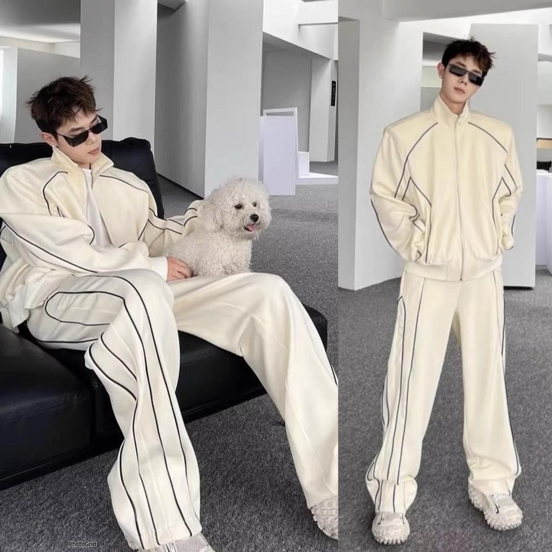 Man modeling cream two-piece tracksuit with black piping details in sitting pose with dog and standing pose.