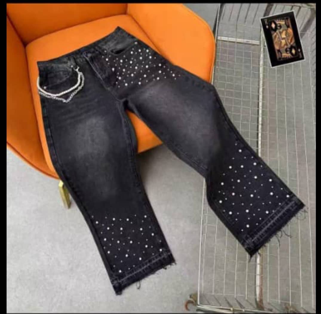 Black baggy jeans with white rhinestone patterns on legs and silver chain, displayed on orange chair.