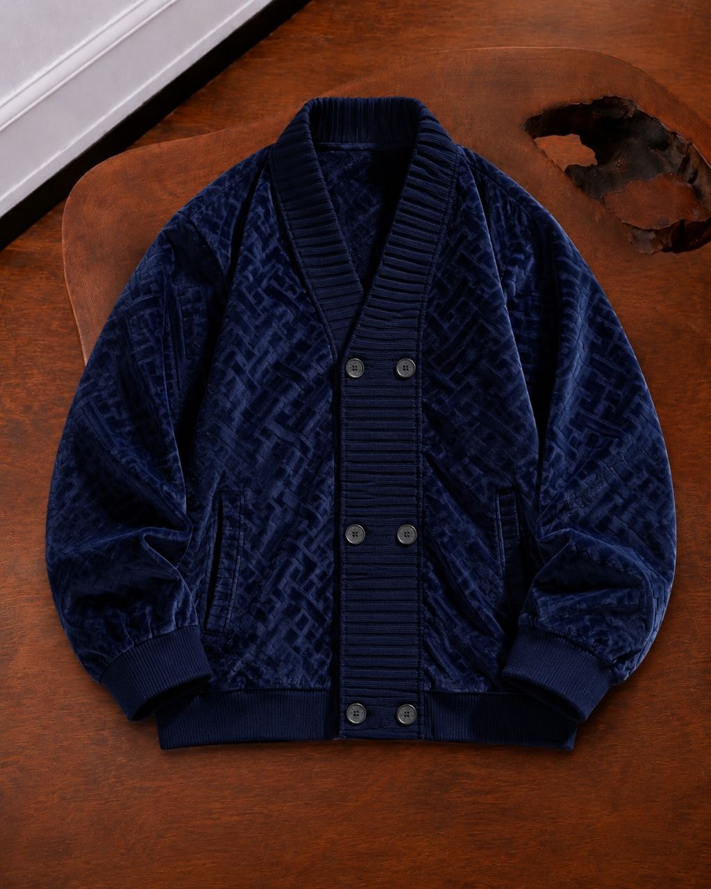Navy geometric patterned velvet bomber jacket laid flat on wooden surface.