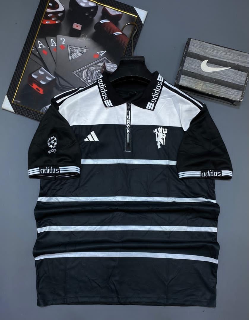 Black and white striped Manchester United Adidas polo jersey laid flat with props.