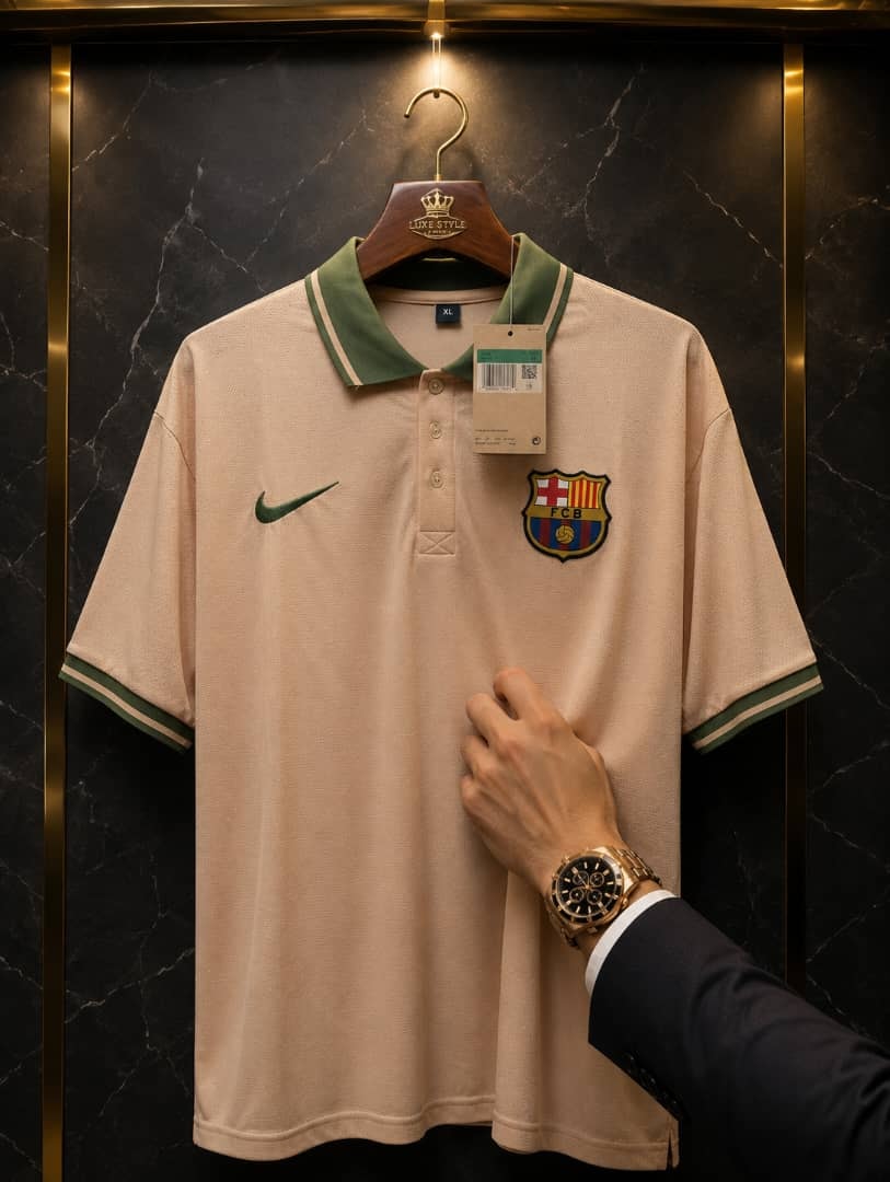 Beige FC Barcelona Nike polo jersey held by a hand against a dark background.