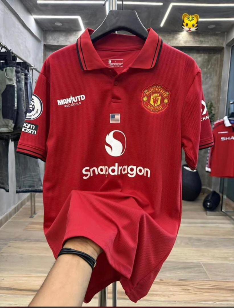 Red Manchester United polo jersey held up in a clothing store.