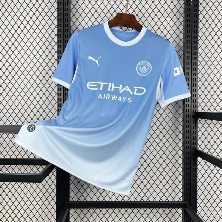 Light blue Manchester City Puma jersey hanging on rack against chain-link fence.
