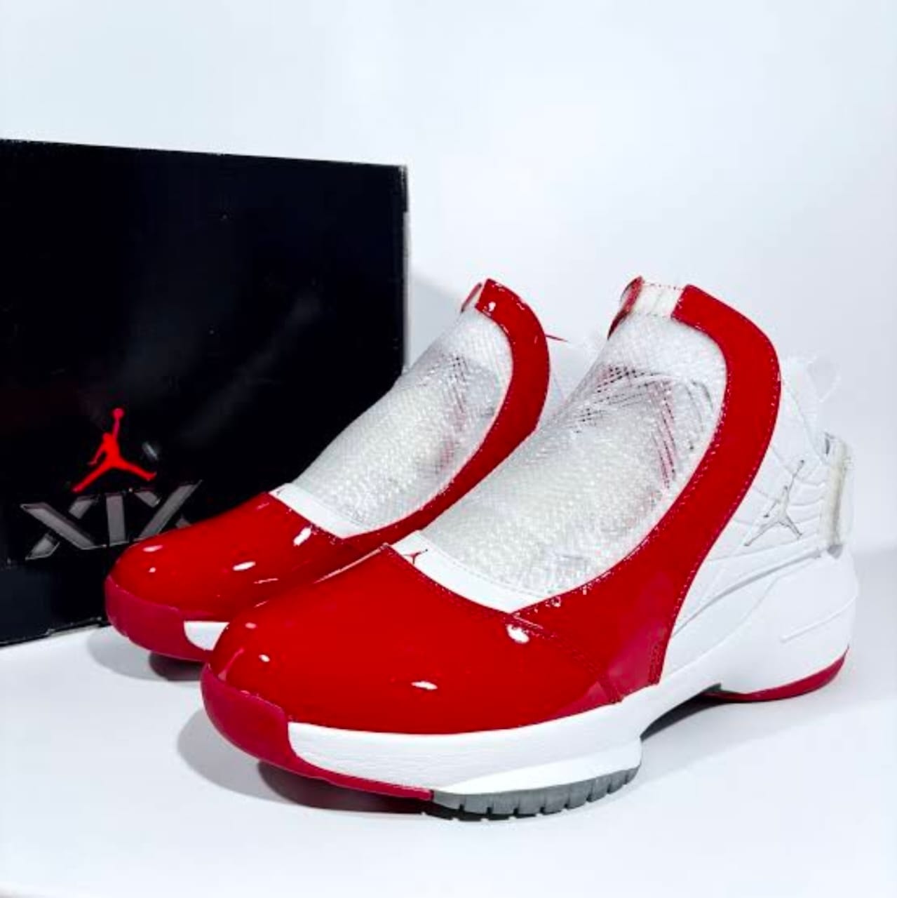 Red and white Jordan sneakers with patent leather, mesh details and black Jordan box in background.