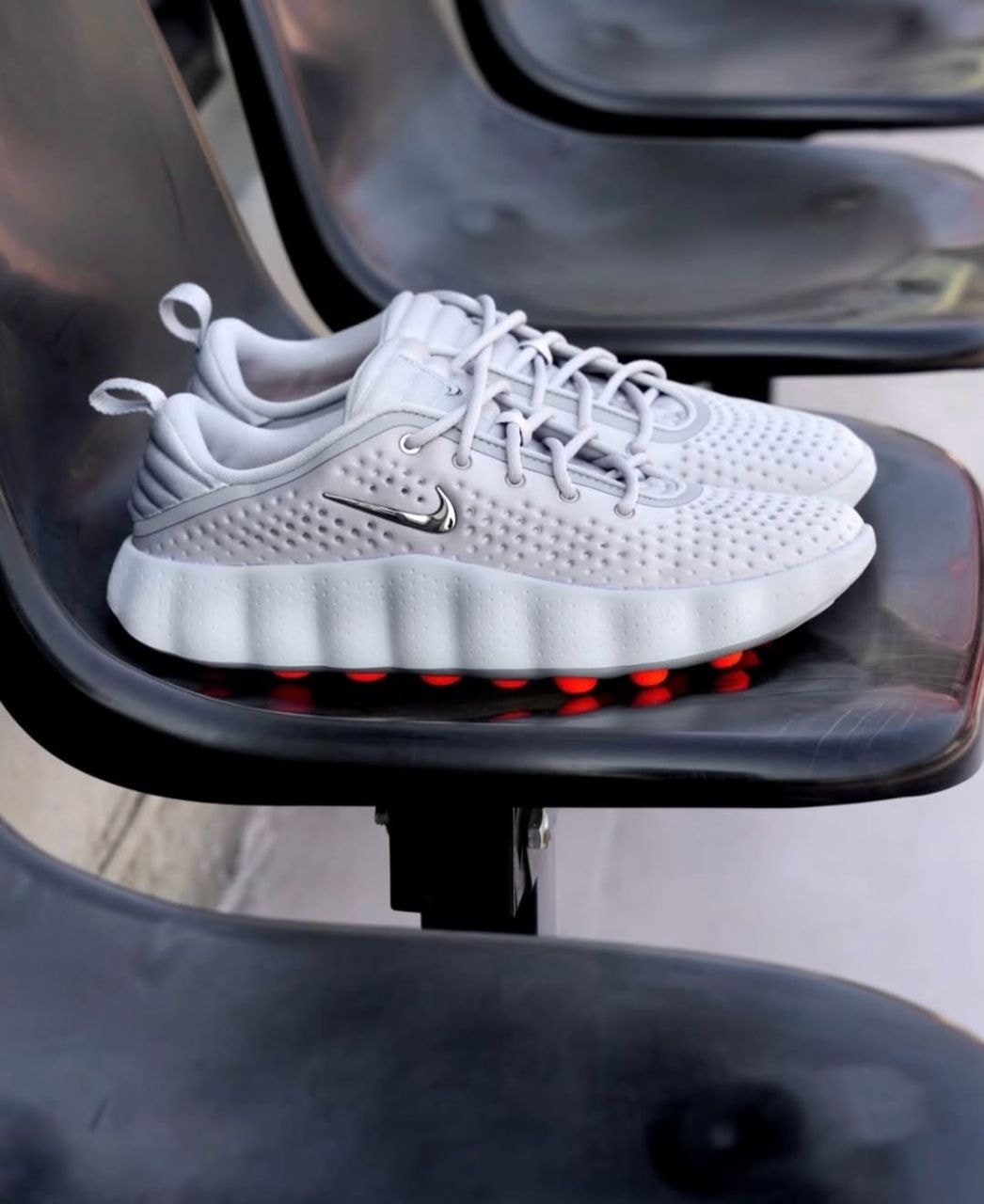 Pair of gray Nike sneakers with orange React pods displayed on black chair.