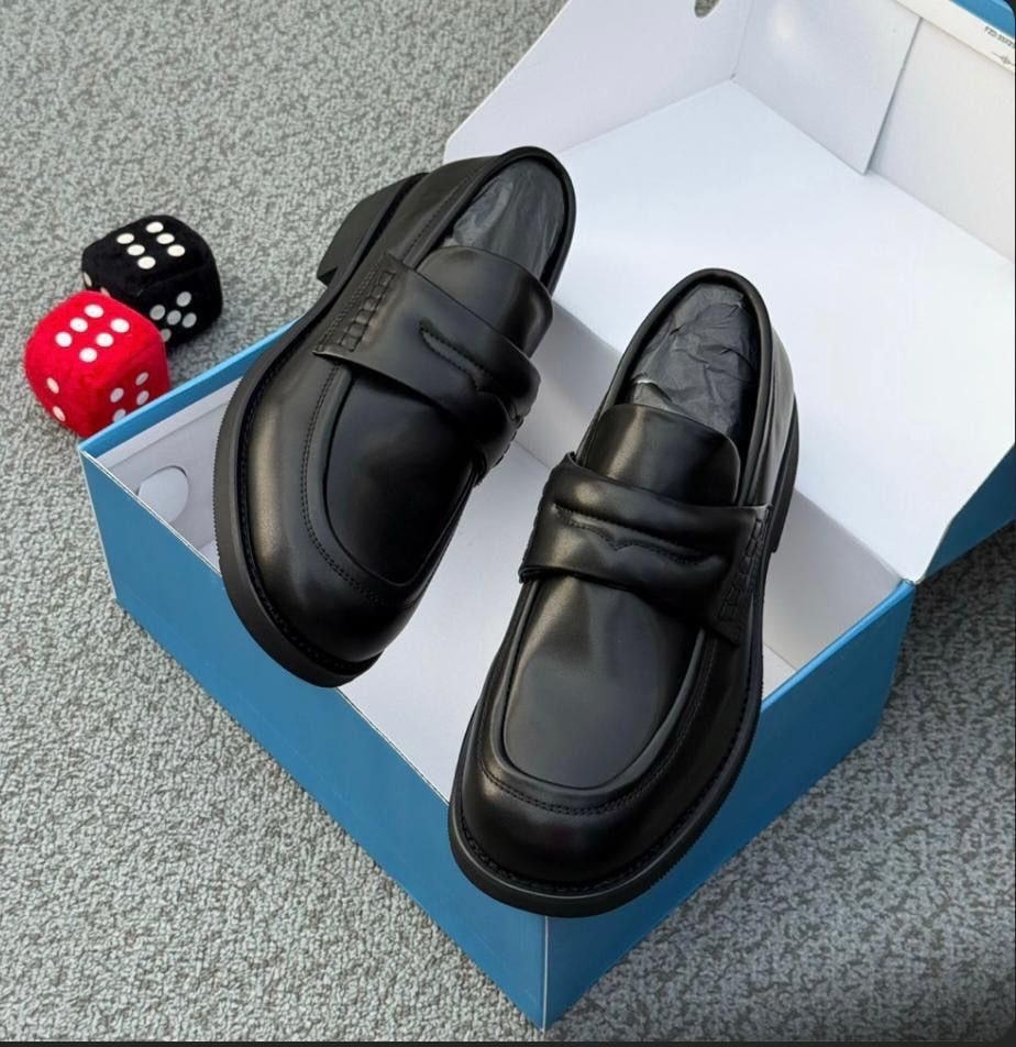 Black leather penny loafers inside an open blue shoebox on carpet.