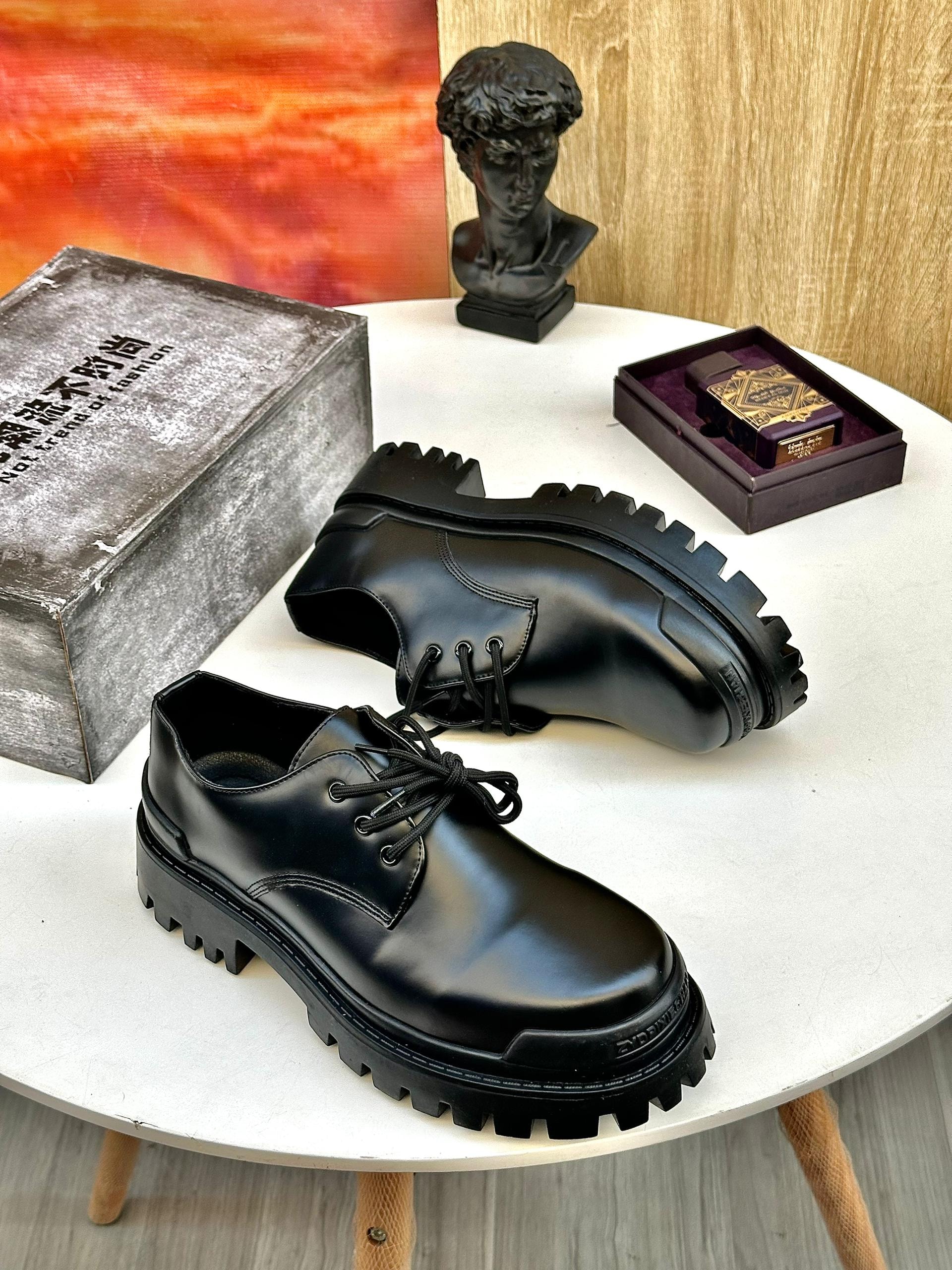 Black chunky lace-up derby shoes with thick tread soles on white table.