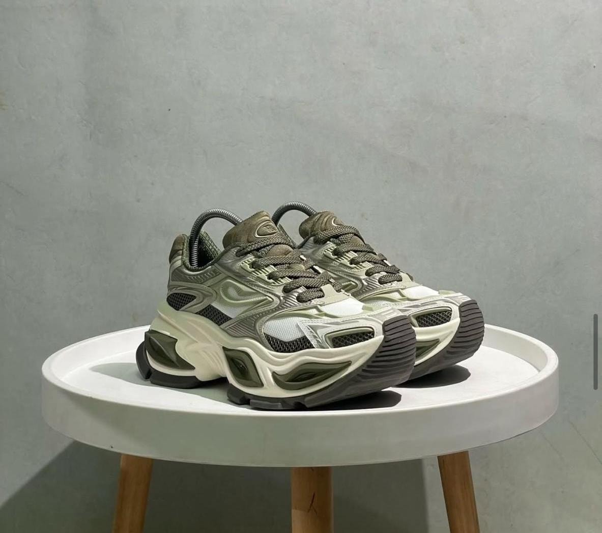 Olive green and white chunky sneakers displayed on a white round table.