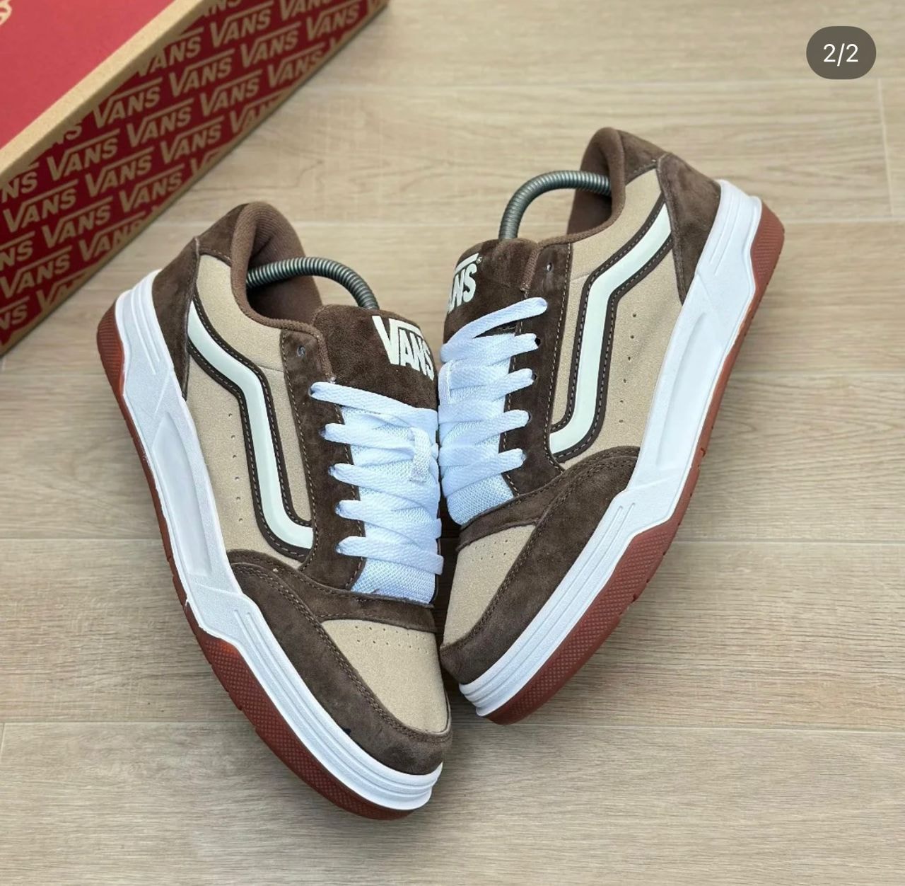 Brown and beige Vans sneakers with white laces and soles next to a branded box.