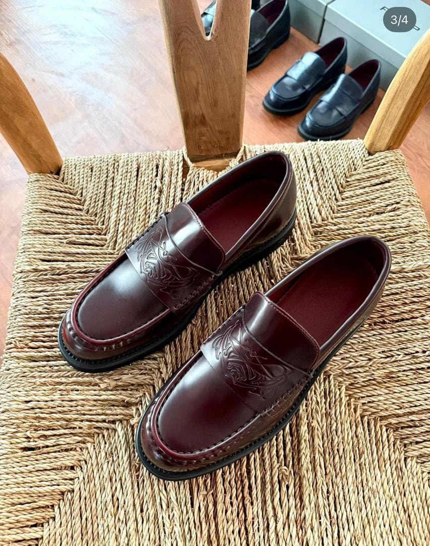 Burgundy leather loafers with embossed details displayed on a woven chair.