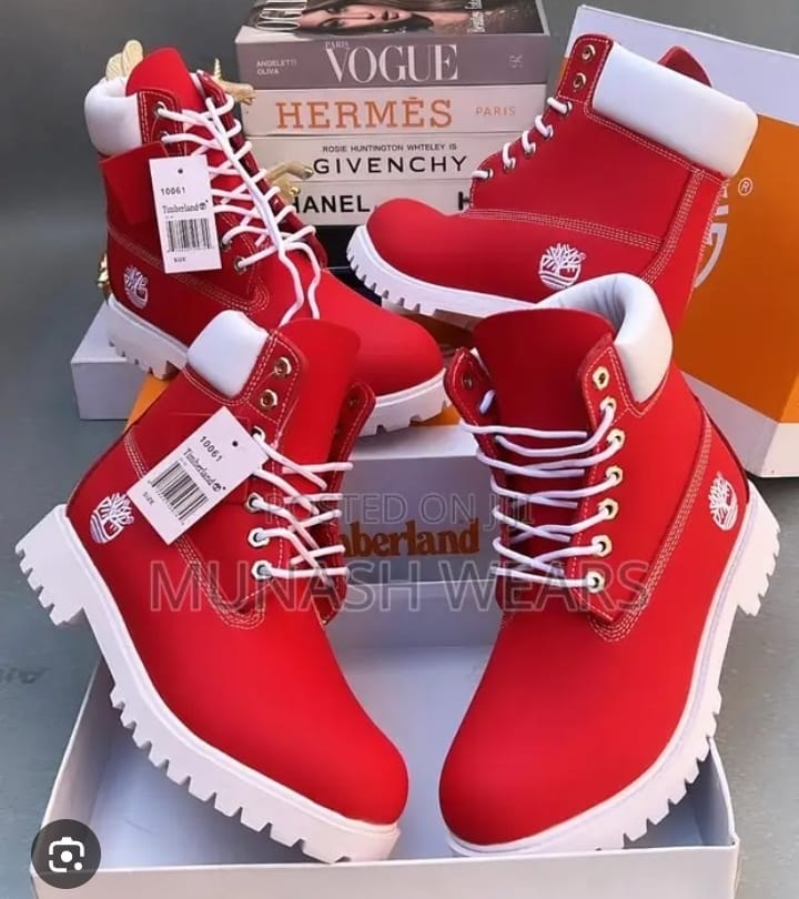Pair of red Timberland boots with white soles and tags displayed on boxes with fashion magazines.
