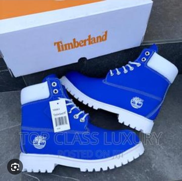 Blue Timberland boots with white soles, logos, and attached tags beside a branded box.