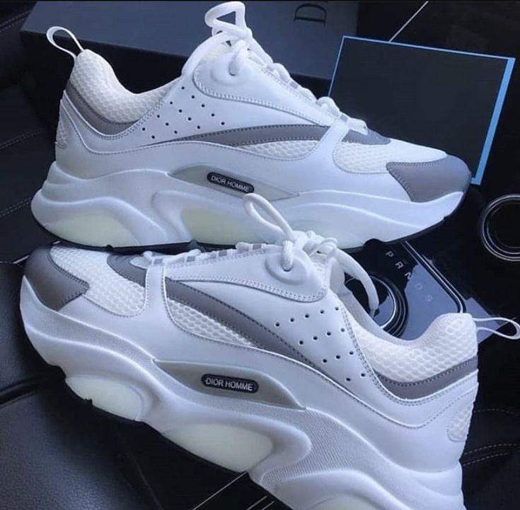 White and grey Dior Homme chunky sneakers with thick sole displayed on car interior.