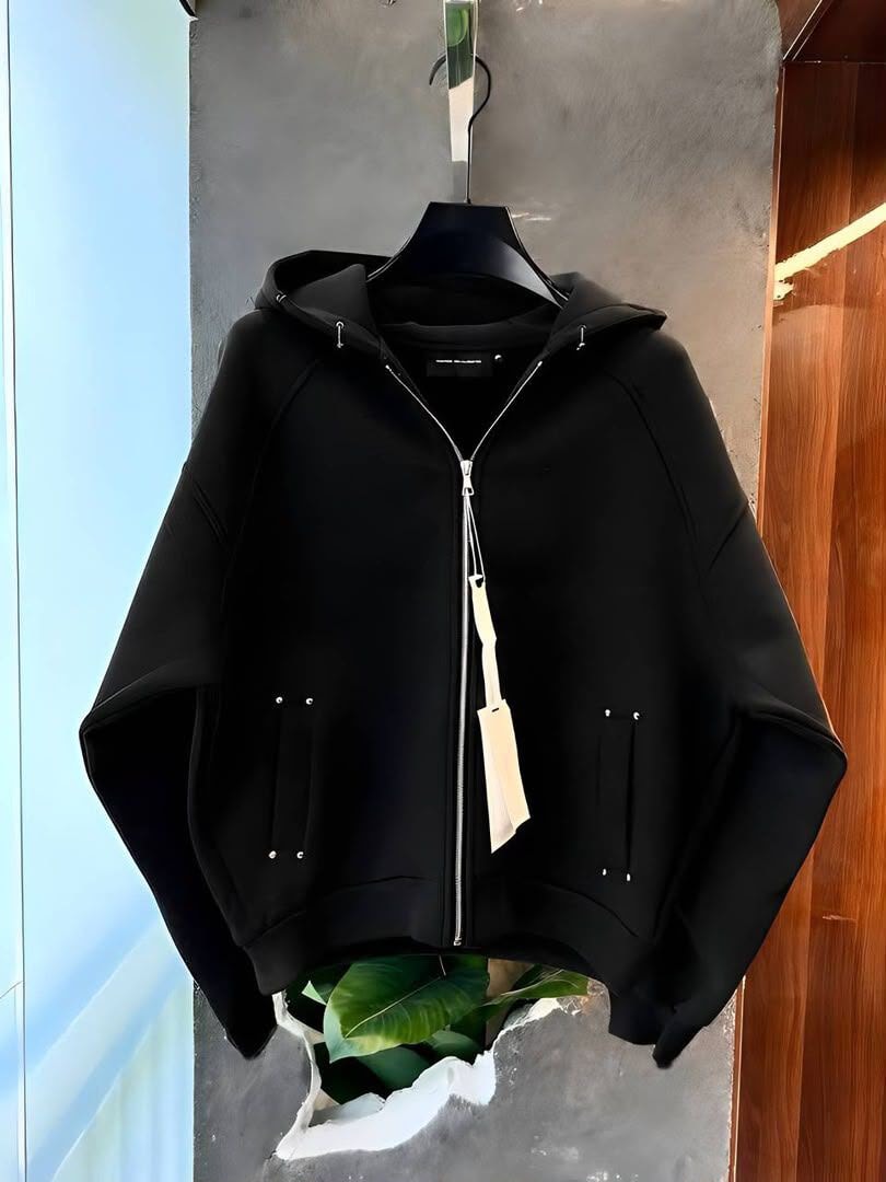 Black zip-up hoodie hanging on black hanger with plant at base.