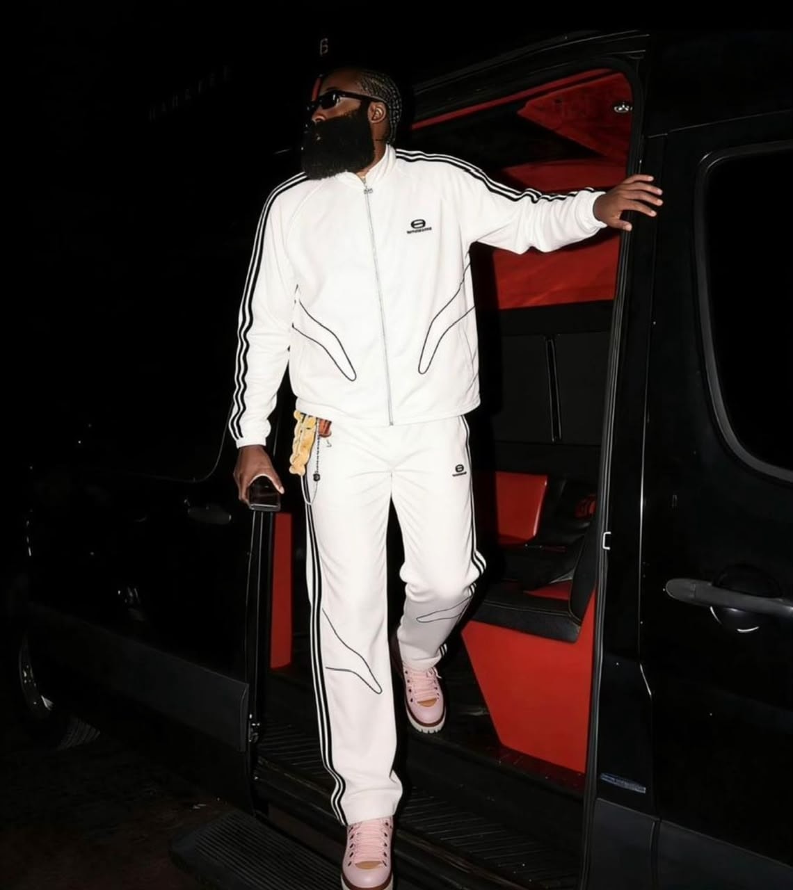 Man in white Balenciaga tracksuit stepping out of a van at night.