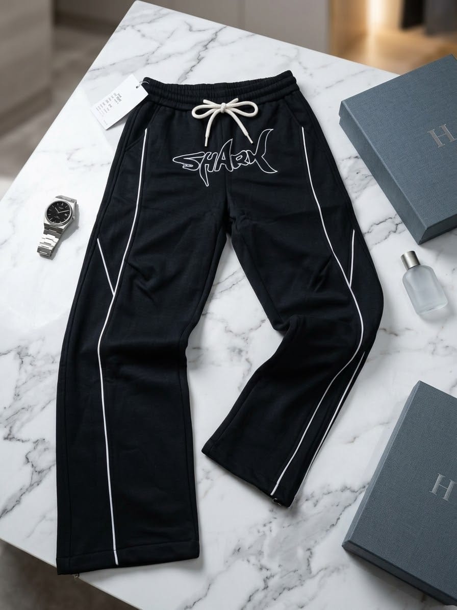 Black joggers with white SHARK graphic and side piping on marble table with accessories.