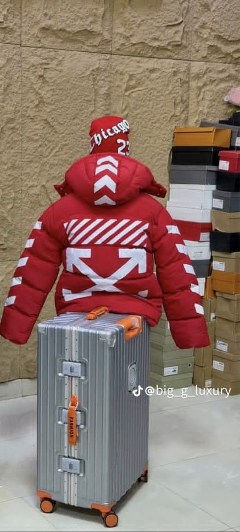 Back view of red puffer jacket with white arrow and chevron graphics on suitcase.