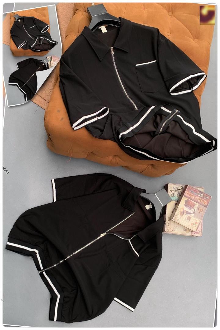 Black short sleeve zip jacket with white contrast trim displayed on orange tufted ottoman and flat lay views.
