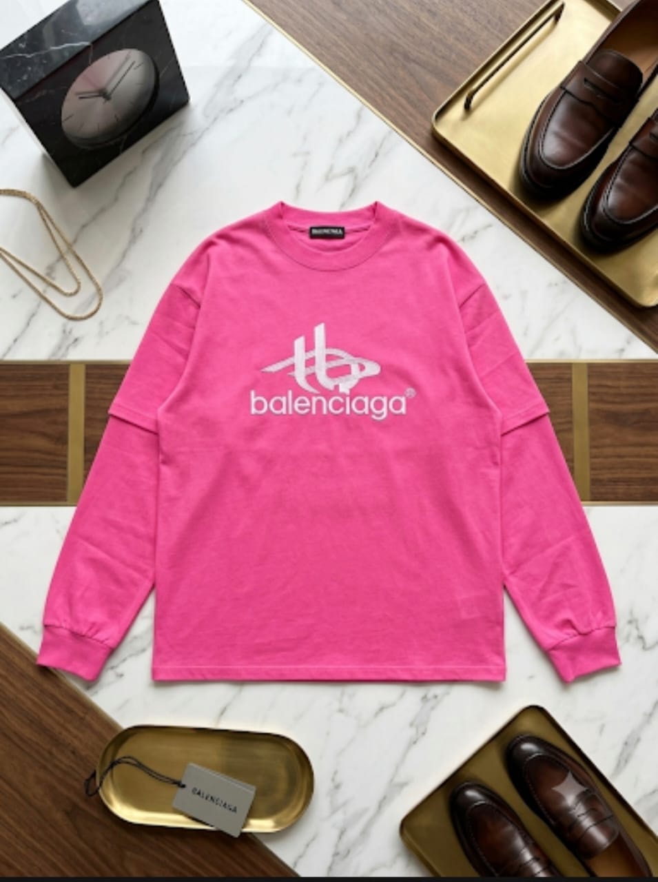 Pink Balenciaga logo sweatshirt displayed on marble background with gold trays and shoes.