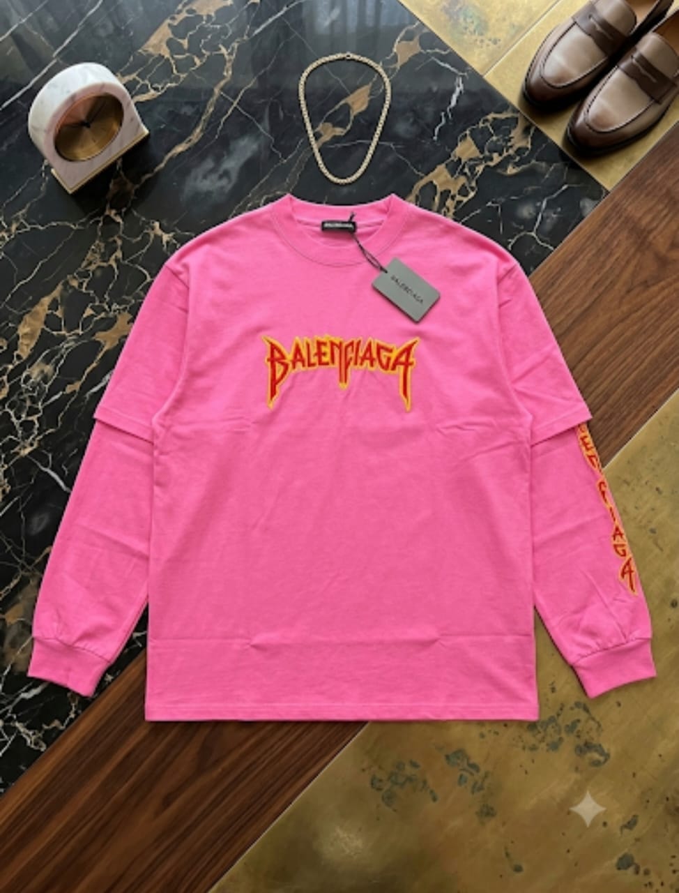 Pink Balenciaga flame print sweatshirt on marble floor with chain and shoes.