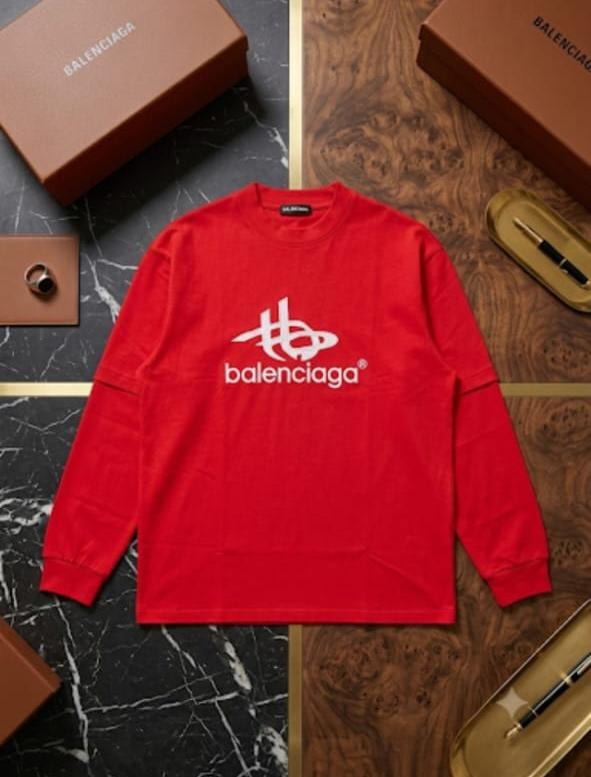 Red Balenciaga logo sweatshirt laid flat on marble and wood surface with accessories.
