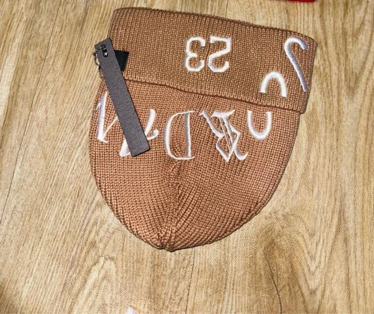 Brown knitted cap with white embroidery laid on wooden surface.