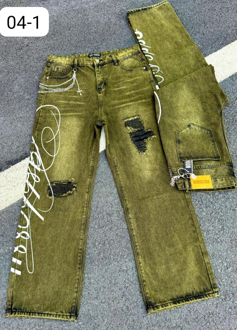 Olive green baggy jeans with white graphics, rips, chains, and cross pendant on pavement.