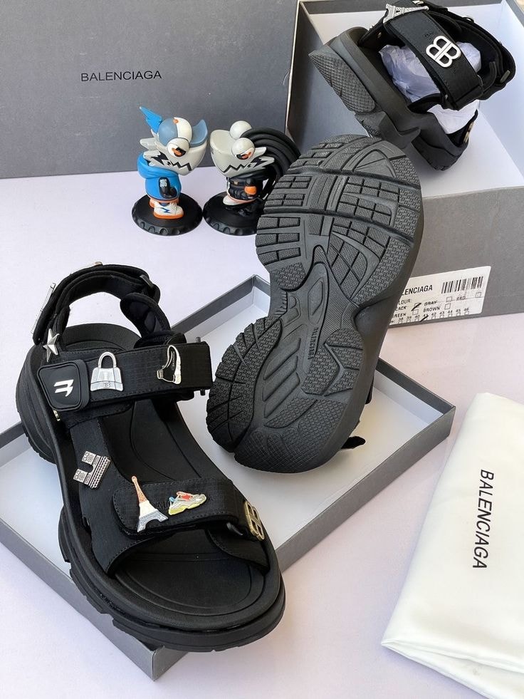 Black Balenciaga sandal with charms and thick sole next to branded box and accessories.