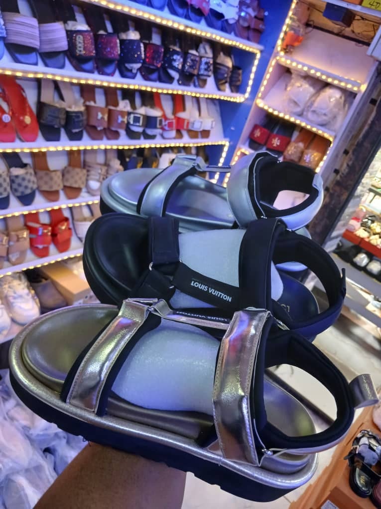 Silver metallic and black Louis Vuitton sandals held in a brightly lit shoe store.