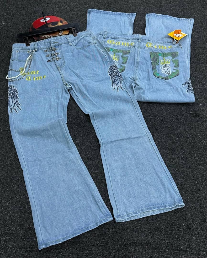 Flat lay of light blue Game Time baggy jeans displaying embroidery, wings, chains and camo skull pockets.