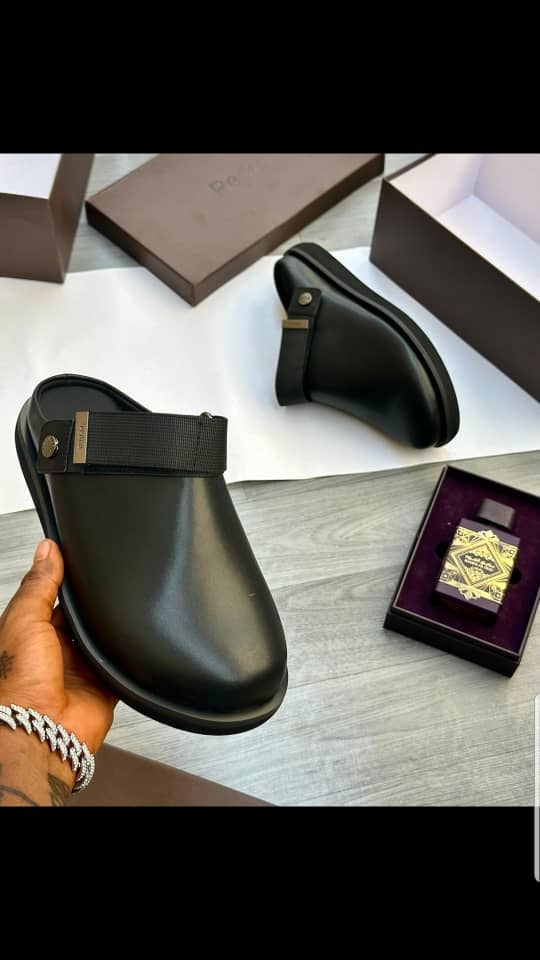 Black Pedro mule with strap held in hand, displayed with boxes and perfume gift set.