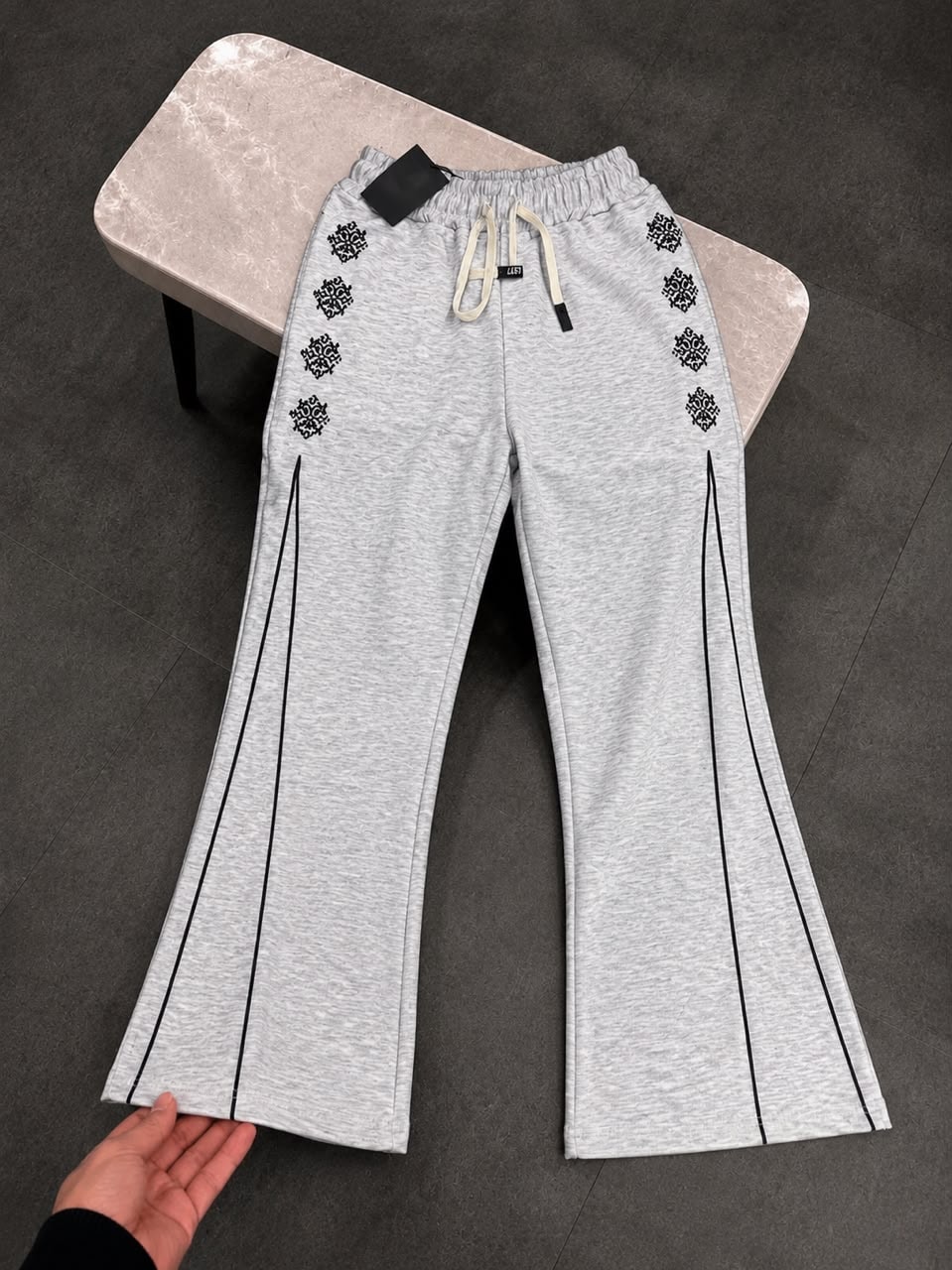Gray joggers with black embroidery and side stripes shown on a table.
