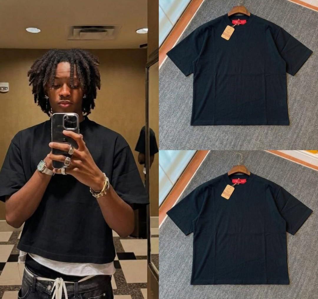 Man in black plain crop tee taking mirror selfie, with black t-shirt flat lays.