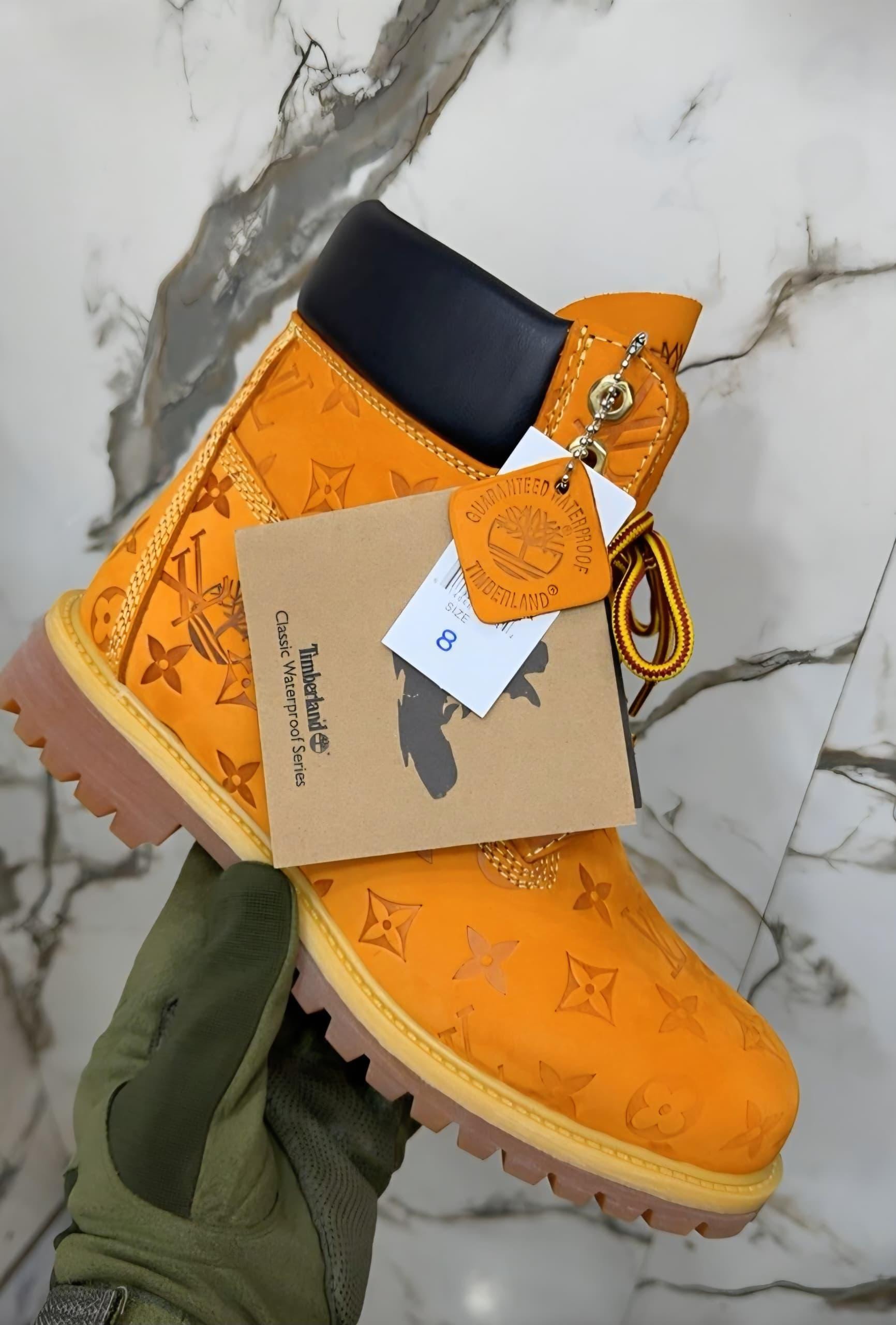 Orange Timberland boots with LV monogram held by gloved hand showing tags and details.