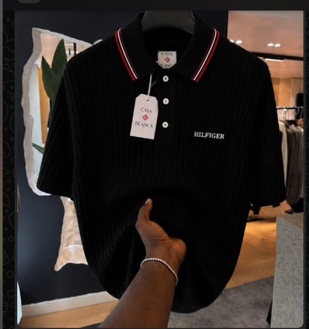 Black ribbed polo shirt with HILFIGER embroidery and striped collar held by hand.