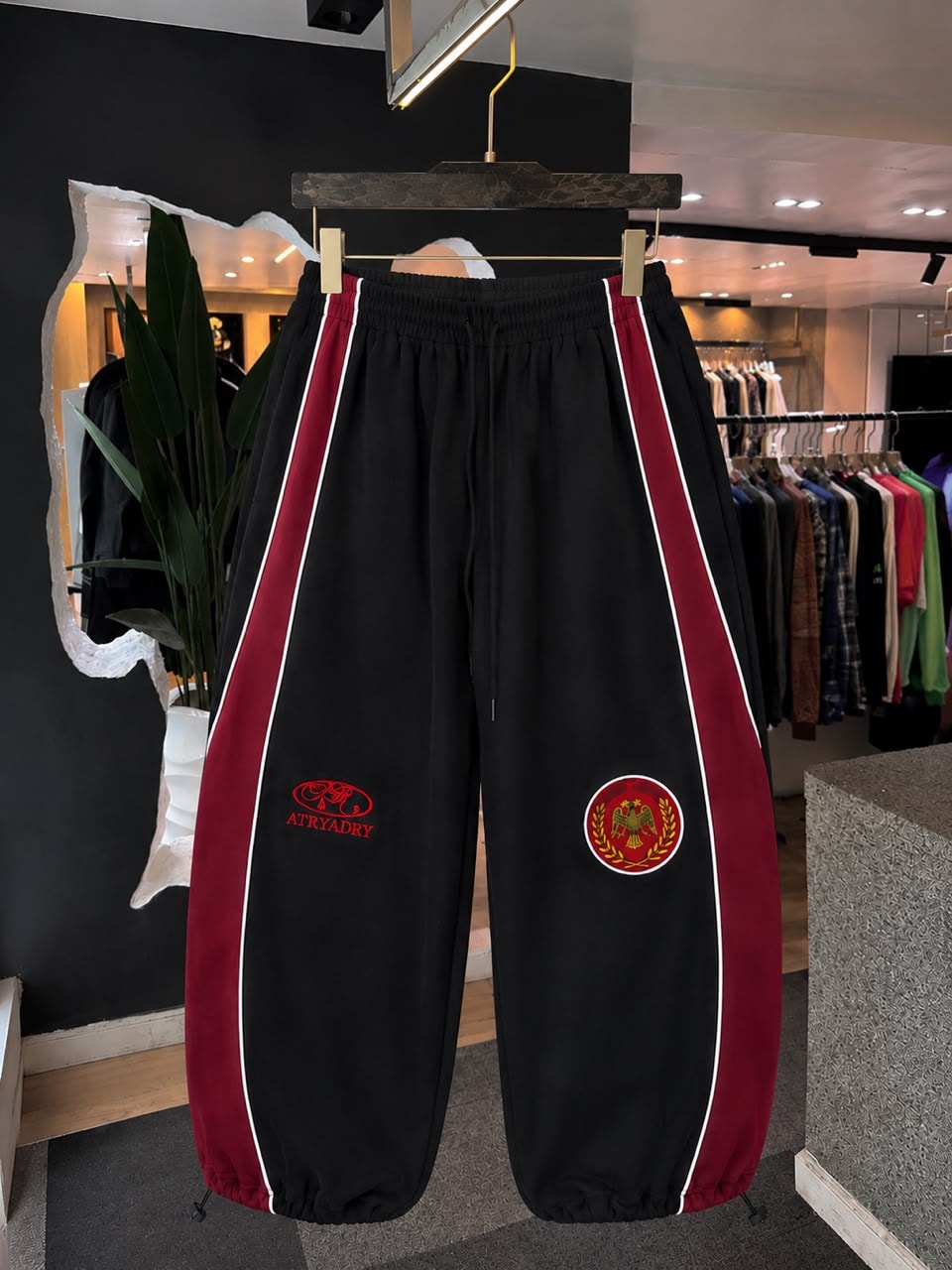 Black Atryadry joggers with burgundy side stripes and red embroidered details.