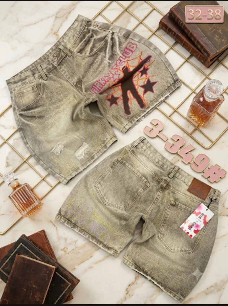 Front and back views of beige distressed denim shorts with graphic print on marble surface with props.