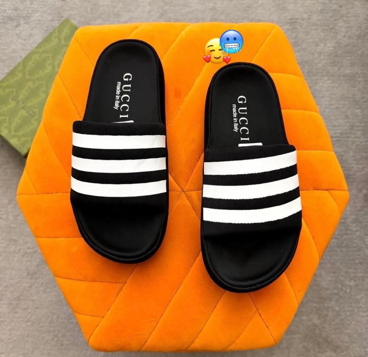 Black Gucci slides with white stripes on orange surface.