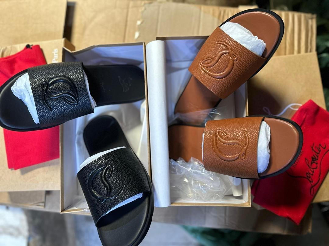 Black and brown Christian Louboutin slides with red dust bags and packaging.