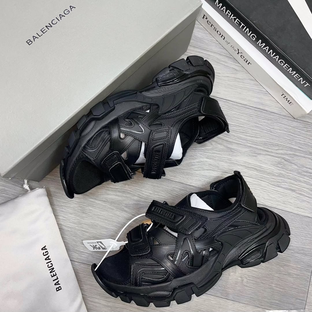 Black Balenciaga multi-strap sandals with box on gray surface.