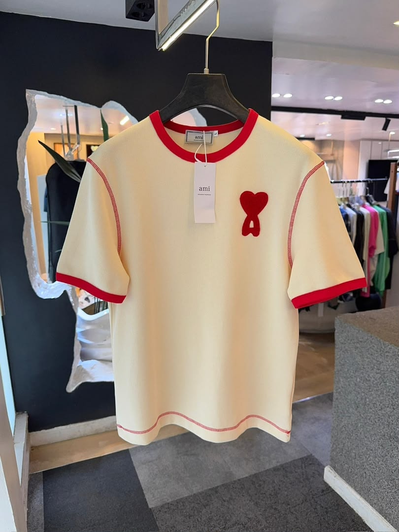 Cream AMI polo shirt with red contrast trim and red heart logo on hanger.